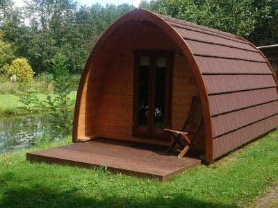 Cabane en bois au bord de leau, avec une terrasse ensoleillée et un cadre verdoyant.