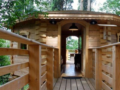 Cabane en bois perchée, avec une belle terrasse en bois entourée darbres verdoyants.