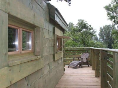 Cabane en bois perchée, avec terrasse en bois et vue sur la nature environnante.