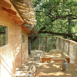 Cabane perchée en bois en Auvergne, avec terrasse en bois entourée darbres.