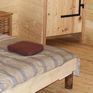 Cabanes en bois en Auvergne, intérieur chaleureux avec lit en bois et chaise pliante.