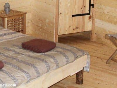 Cabanes en bois en Auvergne, intérieur chaleureux avec lit en bois et chaise pliante.