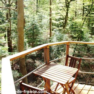 Cabane dans les arbres en Bretagne, avec une terrasse en bois surplombant la forêt verdoyante.