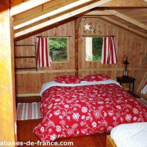 Cabane en bois en Bretagne, avec un lit à baldaquin et des rideaux rayés.