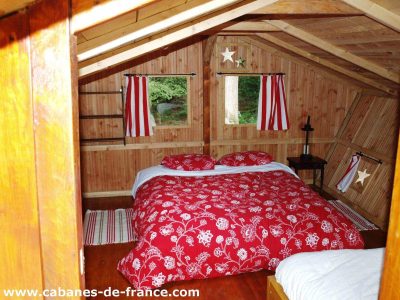 Cabane en bois en Bretagne, avec un lit à baldaquin et des rideaux rayés.