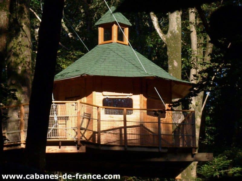 Cabane perchée en bois en Bretagne, avec un toit en pente et une vue sur la forêt.
