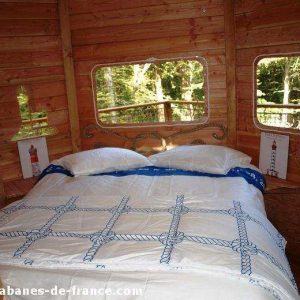 Cabane en bois en Bretagne, avec un lit douillet et de grandes fenêtres.