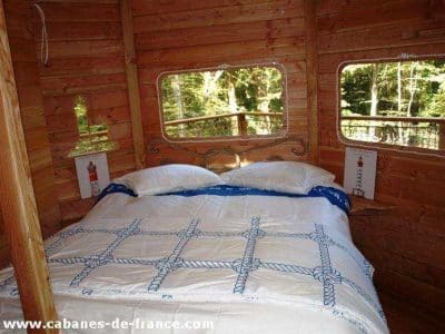 Cabane en bois en Bretagne, avec un lit douillet et de grandes fenêtres.