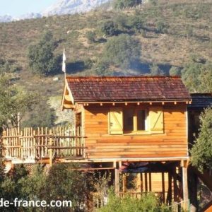 Cabane en bois perchée, entourée de verdure, offrant une vue sur les montagnes corses.
