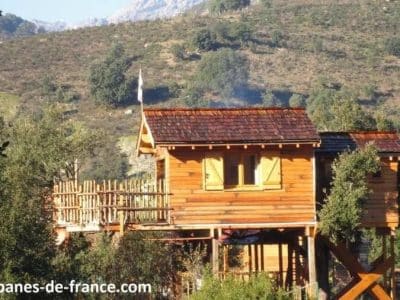 Cabane en bois perchée, entourée de verdure, offrant une vue sur les montagnes corses.