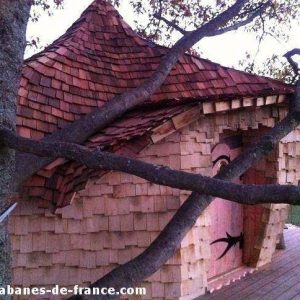 Cabane perchée dans un arbre, toit en ardoise, ambiance nature et paisible.