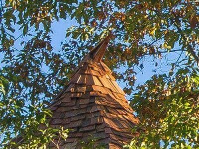 Cabane perchée en bois, toit en ardoise, entourée darbres verdoyants.