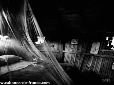 Cabane en bois en Bretagne, lit sous un voile délicat et décor mural artistique.