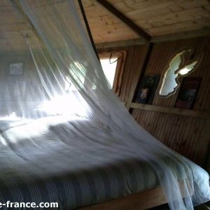 Cabane en bois en Bretagne, lit avec moustiquaire et décor naturel.