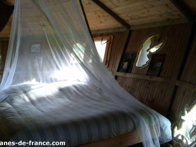 Cabane en bois en Bretagne, lit avec moustiquaire et décor naturel.