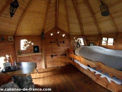 Cabane en bois en Bretagne, intérieur chaleureux avec lit en bois sculpté.
