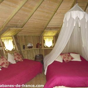 Cabanes en bois en Bretagne, intérieur chaleureux avec lits douillets et rideau en voile.