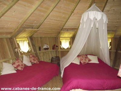 Cabanes en bois en Bretagne, intérieur chaleureux avec lits douillets et rideau en voile.