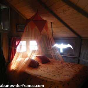 Cabane perchée en Bretagne, lit rond avec voilage orange et vue sur la nature.