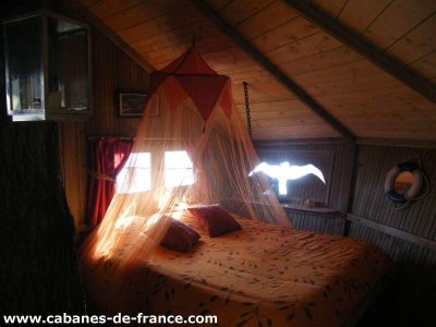 Cabane perchée en Bretagne, lit rond avec voilage orange et vue sur la nature.