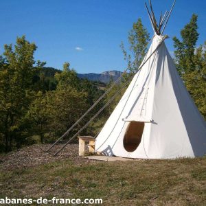 Tipi en pleine nature, entouré darbres et avec des montagnes en arrière-plan.
