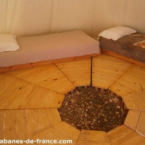 Cabane en bois dans les arbres, avec lits en bois et sol en rondins.