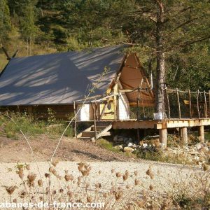 Cabane en bois sur pilotis, entourée de verdure et dune terrasse en bois.