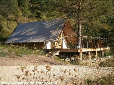 Cabane en bois sur pilotis, entourée de verdure et dune terrasse en bois.
