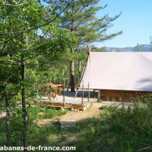 Cabane perchée en bois, entourée de verdure, avec terrasse en bois.