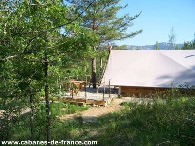 Cabane perchée en bois, entourée de verdure, avec terrasse en bois.