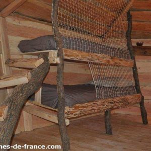 Cabane en bois avec lits superposés en branches, ambiance naturelle et chaleureuse.