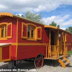 Charmante roulotte rouge avec fenêtres jaunes, entourée de verdure.