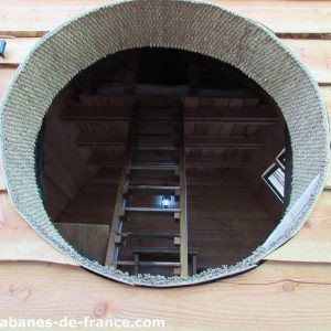 Cabane en bois avec une ouverture ronde et une échelle menant à lintérieur.