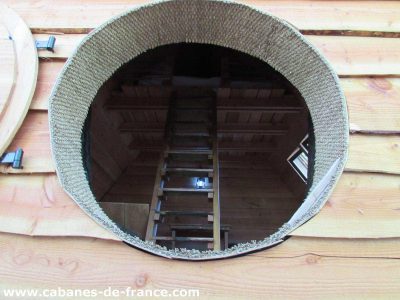 Cabane en bois avec une ouverture ronde et une échelle menant à lintérieur.