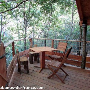 Cabane perchée en bois avec terrasse en bois dans les arbres, entourée de verdure.