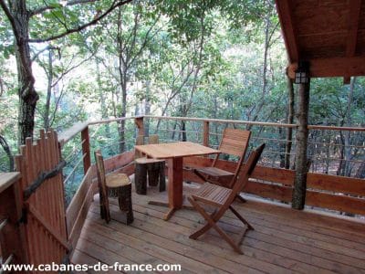 Cabane perchée en bois avec terrasse en bois dans les arbres, entourée de verdure.