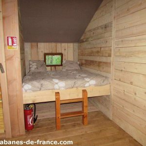Cabane en bois cosy avec lit double et fenêtres donnant sur la nature.
