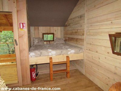 Cabane en bois cosy avec lit double et fenêtres donnant sur la nature.