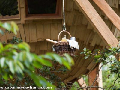 Cabane perchée dans les arbres, panier suspendu avec des douceurs à lentrée.