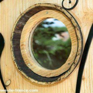 Cabane en bois avec un miroir rond encastré dans la porte, ambiance naturelle.