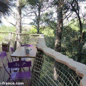 Cabane perchée dans les arbres, avec une terrasse en bois et des chaises violettes.