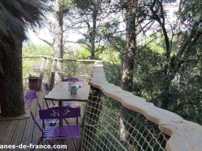 Cabane perchée dans les arbres, avec une terrasse en bois et des chaises violettes.