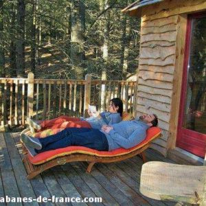 Cabane en bois perchée, avec terrasse en bois et chaises longues confortables.