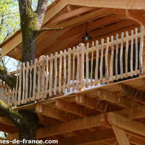 Cabane perchée dans les arbres, avec un balcon en bois et une vue sur la nature.