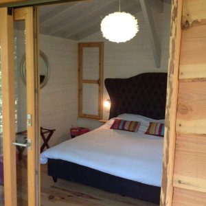 Chambre cocooning dans une cabane en bois, avec un lit confortable et des touches colorées.