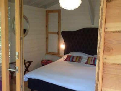 Chambre cocooning dans une cabane en bois, avec un lit confortable et des touches colorées.