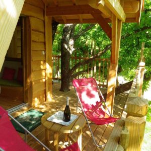 Cabane perchée en Aquitaine, avec terrasse en bois et chaises confortables.