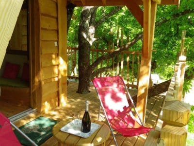 Cabane perchée en Aquitaine, avec terrasse en bois et chaises confortables.