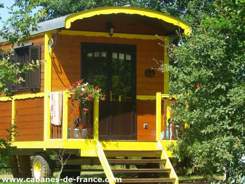 Charmante roulotte colorée avec balustrade jaune, nichée dans la verdure dAquitaine.