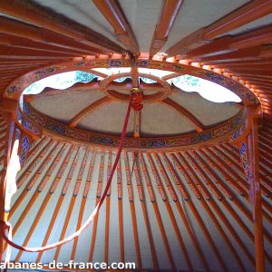 Intérieur dune yourte colorée en Auvergne-Rhône-Alpes, avec un plafond en bois décoré.